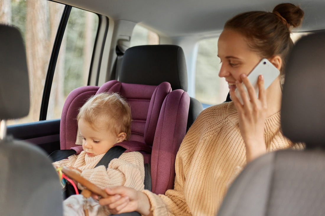 copilul se joaca in scaun auto, alaturi mama vorbeste la telefon