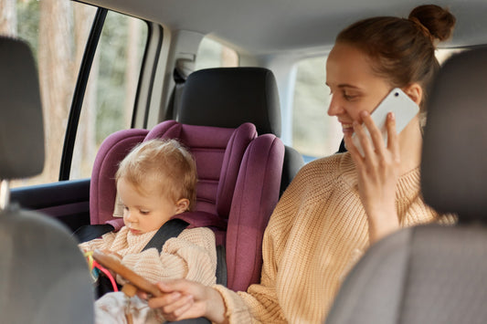 copilul se joaca in scaun auto, alaturi mama vorbeste la telefon
